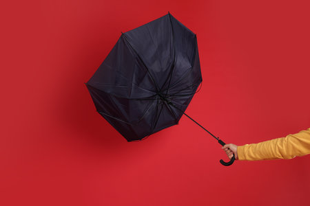 Man holding umbrella caught in thick of wind on red background, closeupの写真素材