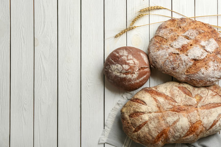 Different kinds of delicious bread on white wooden table, flat lay. Space for textの写真素材