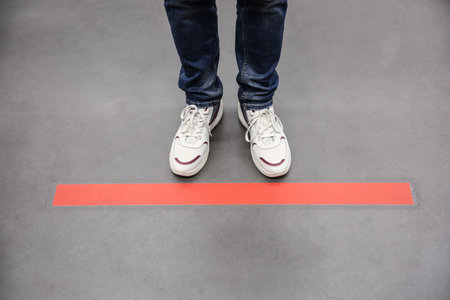 Person standing behind taped floor marking indoors for social distance, closeup. Preventive measure...