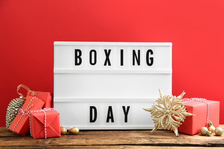 Composition with Boxing Day sign and Christmas gifts on wooden table against red backgroundの写真素材