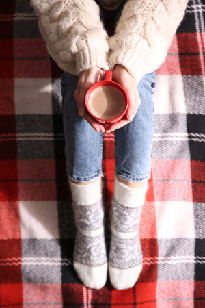 Woman relaxing with cup of hot winter drink on checkered plaid, top viewの写真素材