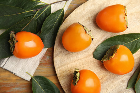 Delicious fresh persimmons and green leaves on wooden table, flat layの写真素材