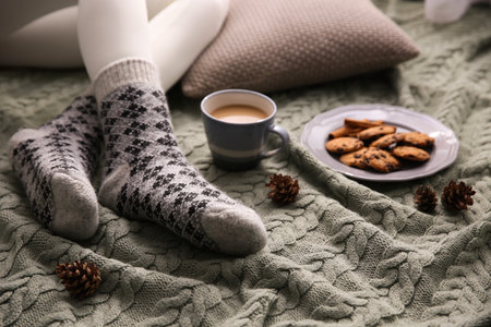Woman wearing warm socks on knitted plaid, closeup. Cozy seasonの写真素材
