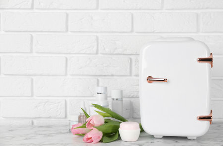 Cosmetic refrigerator and skin care products on white marble table, space for textの写真素材