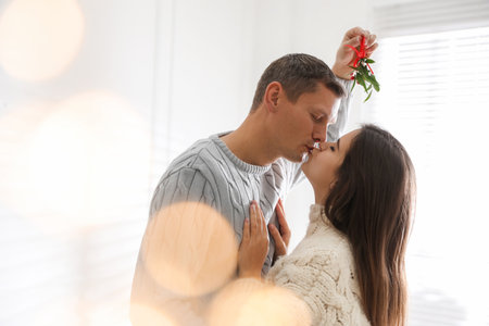 Happy couple kissing under mistletoe bunch at home, bokeh effectの写真素材