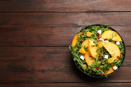 Delicious persimmon salad with pomegranate and arugula on wooden table, top view. Space for textの写真素材