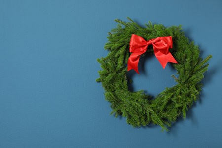 Christmas wreath made of fir branches with red bow on blue wall. Space for textの写真素材