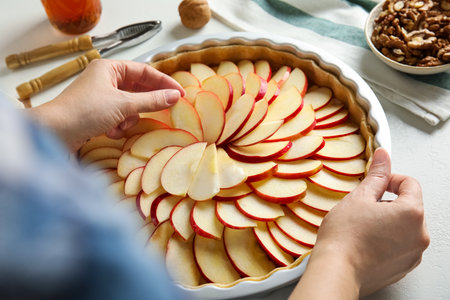 Woman putting apple slices into baking dish with dough to make traditional English pie at white table, closeupの写真素材