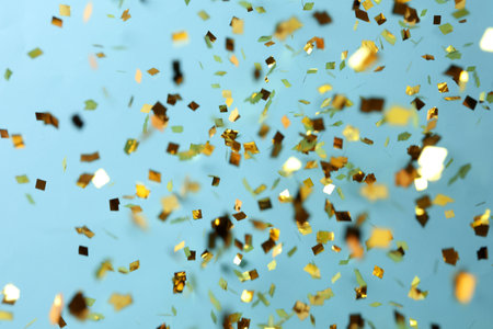 Shiny golden confetti falling down on light blue backgroundの写真素材