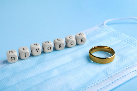Wooden cubes with word Divorce, wedding ring and medical mask on light blue background, closeup.の写真素材