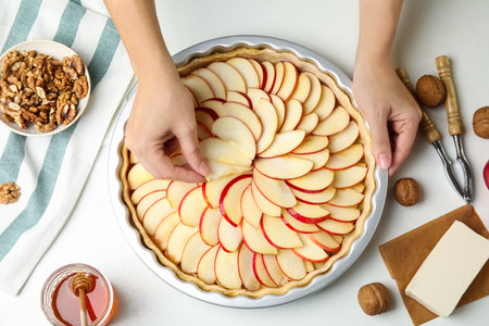Woman apple slice into baking dish with putting dough to make traditional English pie at white table, top viewの写真素材