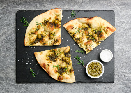 Delicious focaccia bread with green olives on gray table, flat lay