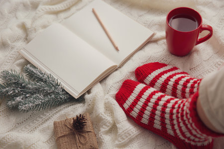Woman with cup of hot winter drink and notebook on knitted plaid, closeup. Cozy seasonの写真素材