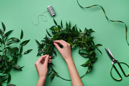 Florist making beautiful mistletoe wreath on green background, top view. Traditional Christmas decorの写真素材