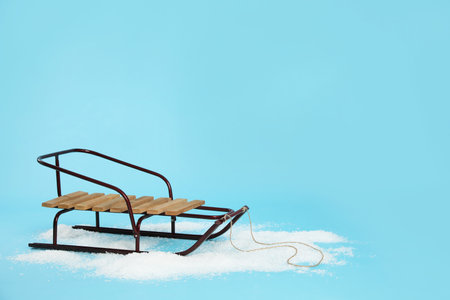 Stylish sleigh in pile of snow on light blue background, space for textの写真素材