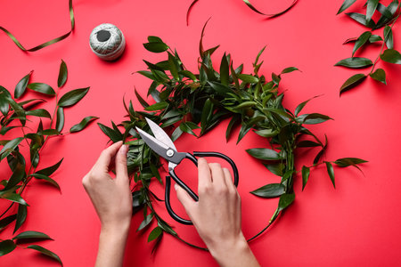Florist making beautiful mistletoe wreath on red background, top view. Traditional Christmas decorの写真素材