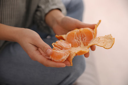 Woman peeling fresh tangerine on blurred background, closeupの写真素材