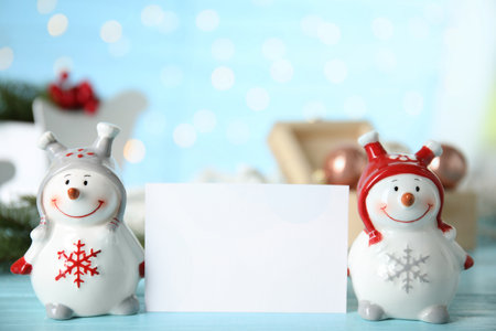 Decorative snowmen near blank white card on light blue table, space for textの写真素材
