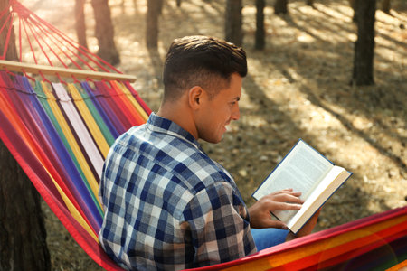 Man with book relaxing in hammock outdoors on summer dayの写真素材