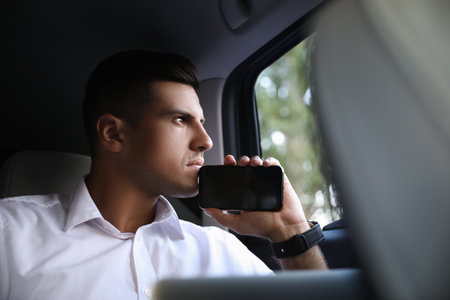 Handsome man with smartphone on backseat of modern car
