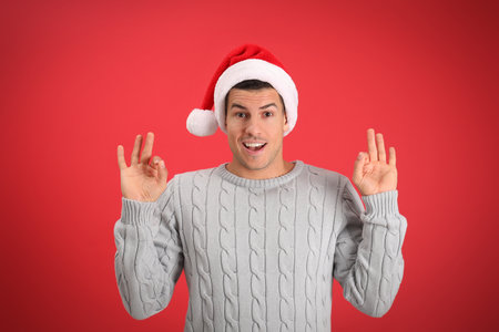 Emotional man wearing Santa hat on red backgroundの写真素材