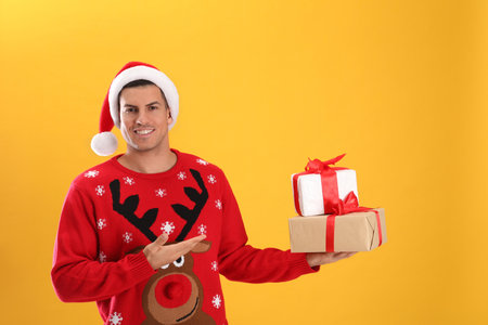 Handsome man in Santa hat holding gift boxes on yellow backgroundの写真素材