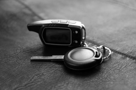 Modern car key with remote control on black leather, closeup