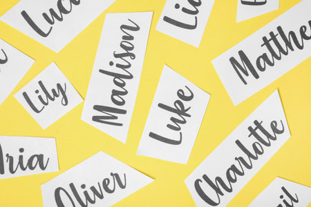 Paper sheets with written different baby names on yellow background, flat layの写真素材