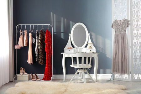 Rack with collection of festive beautiful clothes and dressing table in stylish room interiorの写真素材