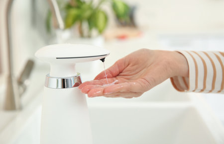 Woman using automatic soap dispenser in kitchen, closeupの写真素材