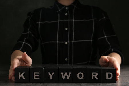 Woman demonstrating black cubes with word KEYWORD at gray table, closeupの写真素材