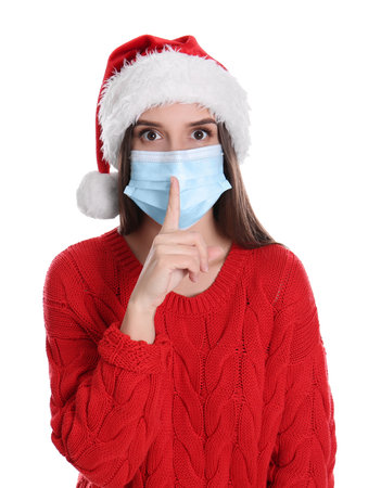 Pretty woman in Santa hat and medical mask showing silence gesture on white backgroundの写真素材