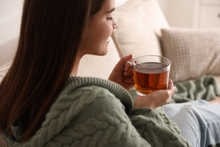 Woman covered with warm green plaid enjoying hot tea at homeの写真素材