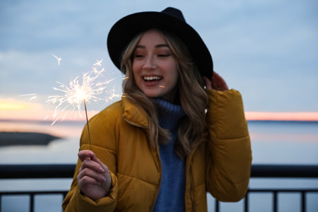 Woman in warm clothes holding burning sparkler near riverの写真素材