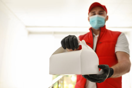 Courier in protective mask and gloves with order indoors, focus on hands. Restaurant delivery service during quarantineの写真素材