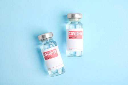 Vials with coronavirus vaccine on light blue background, flat layの写真素材