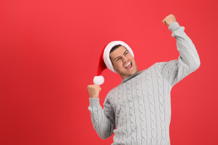 Excited man wearing Santa hat on red background, space for textの写真素材