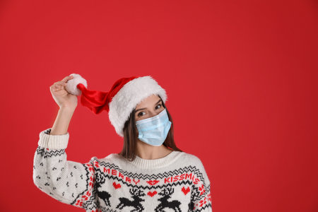 Pretty woman in Santa hat and medical mask on red background, space for textの写真素材