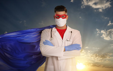 Medical workers fighting dangerous diseases. Doctor dressed as superhero posing against skyの写真素材