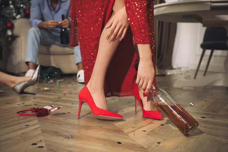Woman with bottle of alcohol in messy room after New Year party, closeup of legsの写真素材