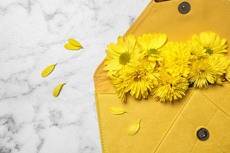 Beautiful women's clutch and chrysanthemum flowers on white marble background, flat lay. Space for textの写真素材