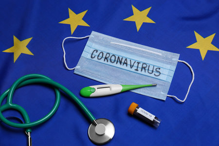 Stethoscope, medical mask with word Coronavirus, thermometer and test tube on flag of European Unionの写真素材