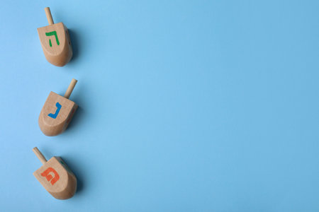 Hanukkah traditional dreidels with letters He, Pe and Nun on light blue background, flat lay. Space for textの写真素材