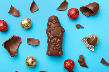 Flat lay composition with whole and broken chocolate Santa Claus candies on light blue backgroundの写真素材