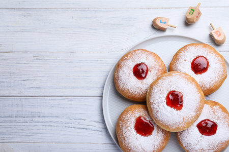 Hanukkah donuts with jelly and sugar powder near dreidels on white wooden table, flat lay. Space for text.の写真素材