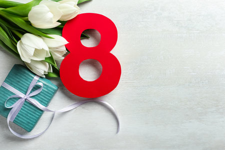 8 March greeting card design with tulips and gift on white wooden table, flat lay. Space for textの写真素材