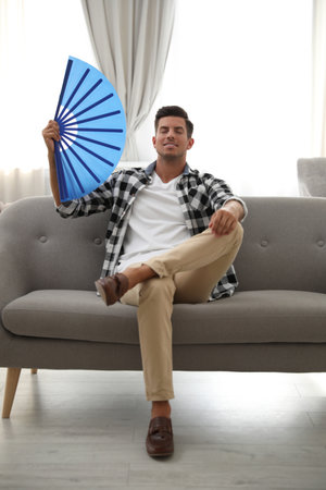 Man with hand fan sitting on sofa. summer seasonの写真素材