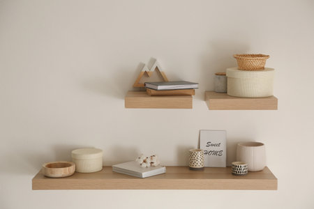 Wooden shelves with books and different decorative elements on light wallの写真素材