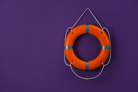Orange lifebuoy and space for text on violet background. Rescue equipment