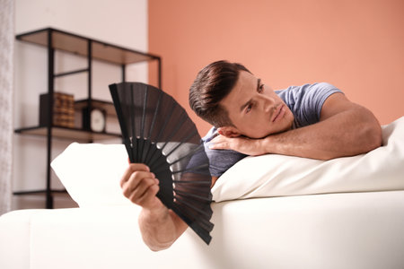 Man with hand fan on sofa. summer seasonの写真素材